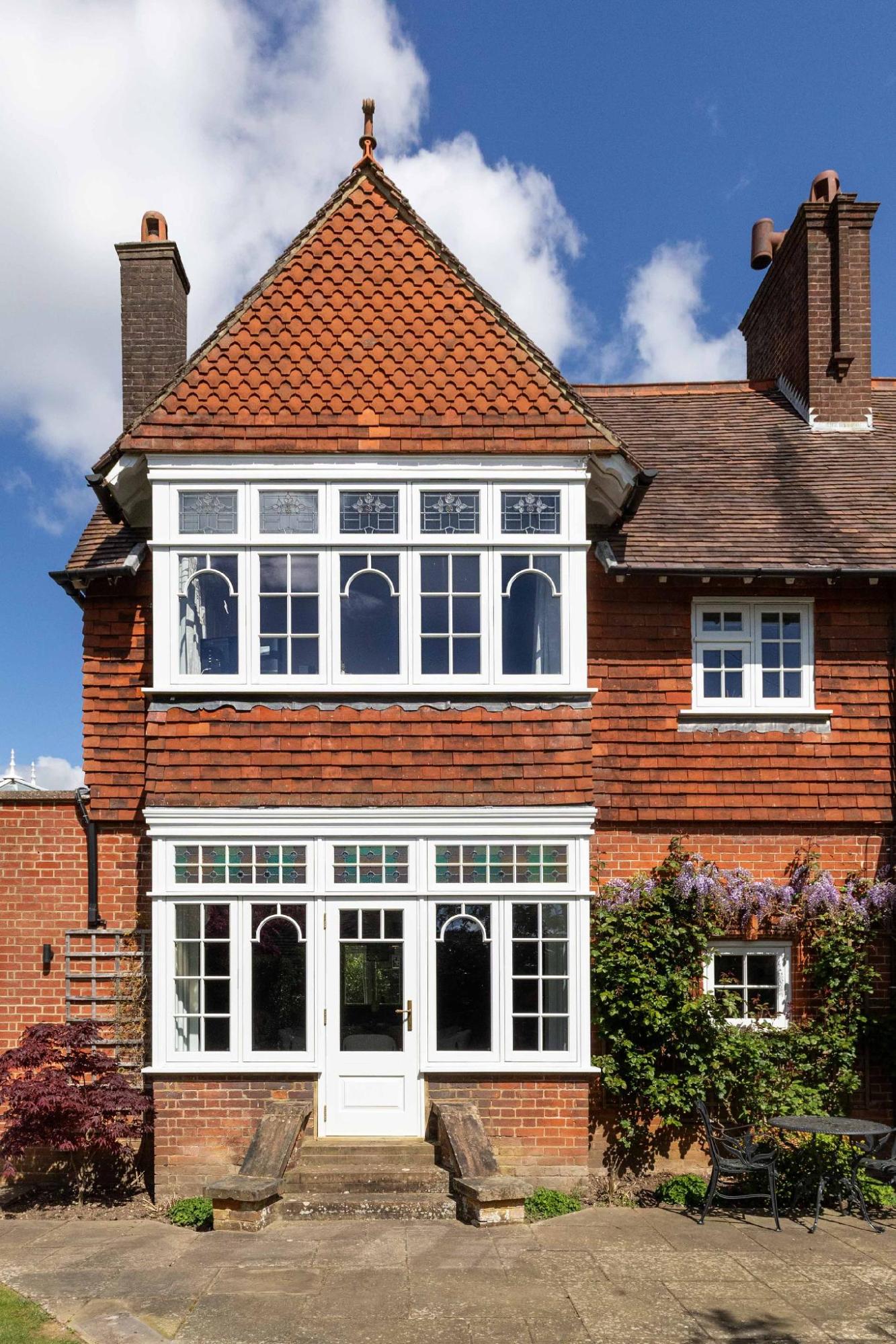white timber bay windows outside with stained glass, red brick, wisteria and blue skies