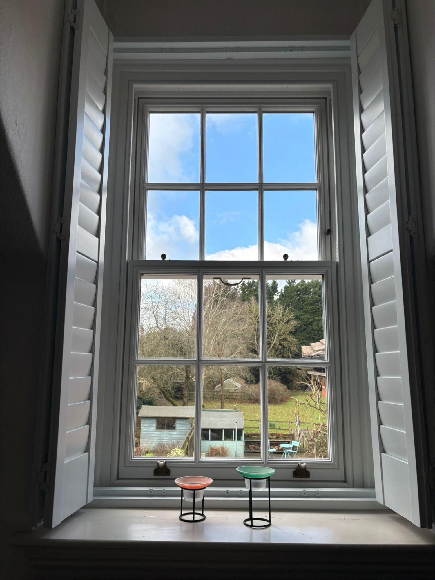 white timber window sliding sash window inside with white shutters looking out to blue skies and garden