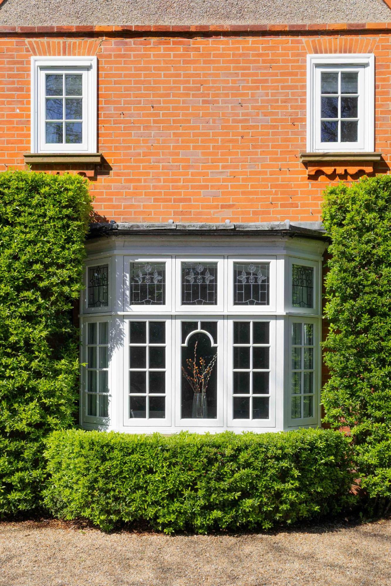 white timber bay window with custom glazing and green hedges